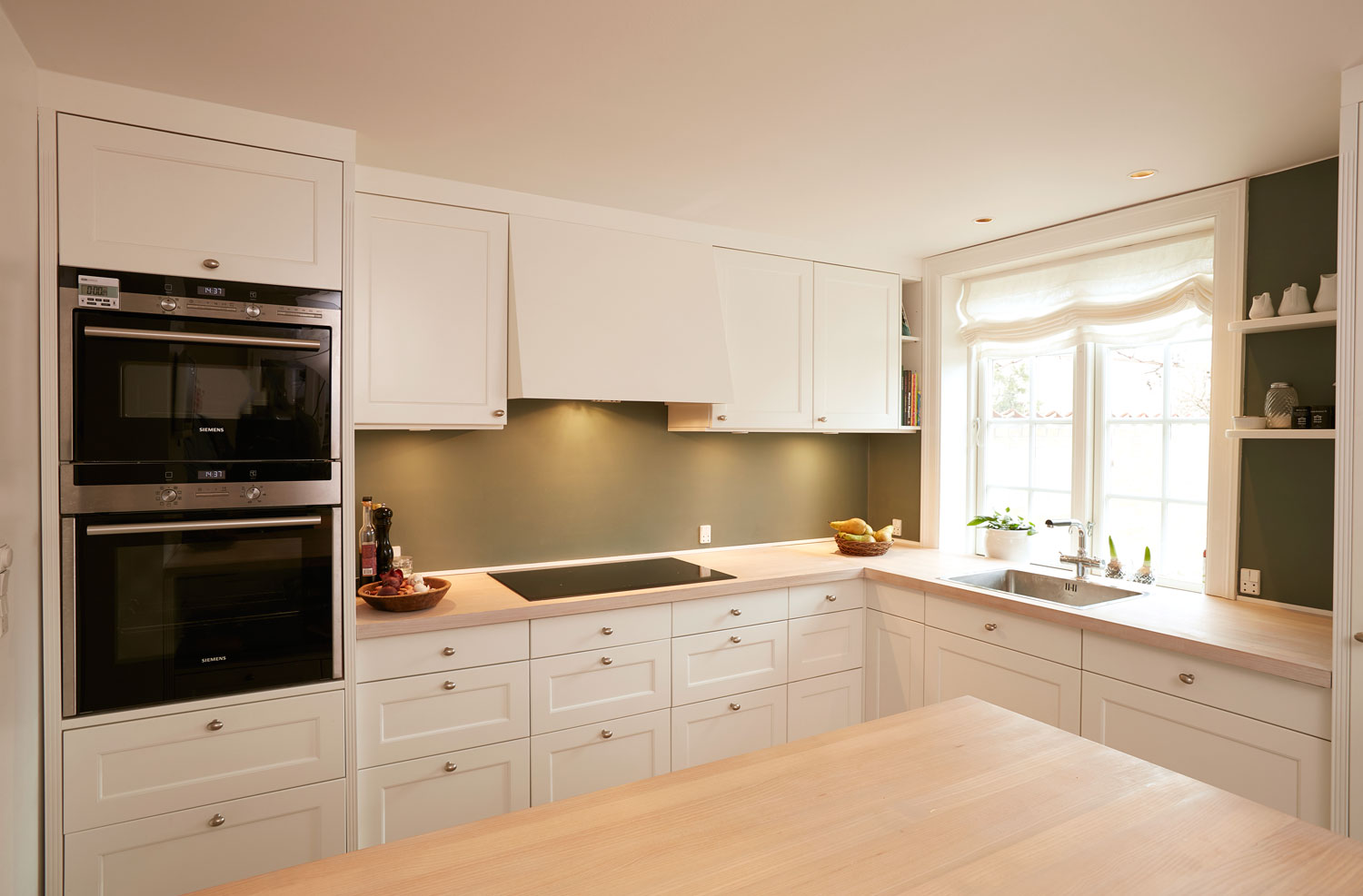 De hvidmalede elementer og bordpladerne i hvidpigmenteret ask får et fint modspil af væggens grønne nuance.